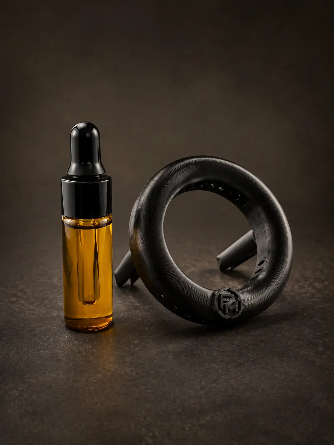 Black Floamen ring with two rear mounting legs beside a fragrance oil dropper bottle