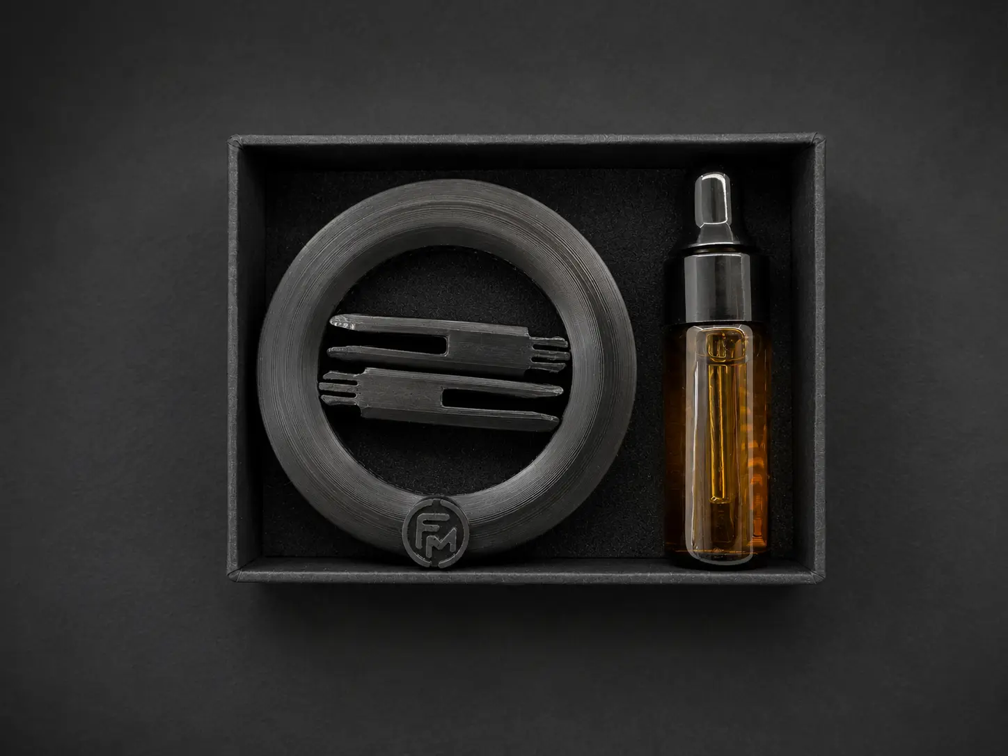 Black presentation box holding the Floamen diffuser, two detached mounting legs inside the ring and a 5 ml fragrance oil bottle